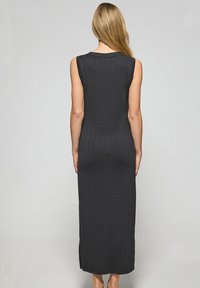 Ärmlös, figurnära svart maxiklänning med vertikala ribbor, som når halvvägs ner på vadder. Mjuk, elastisk tyg, minimal urringning och avslutning.