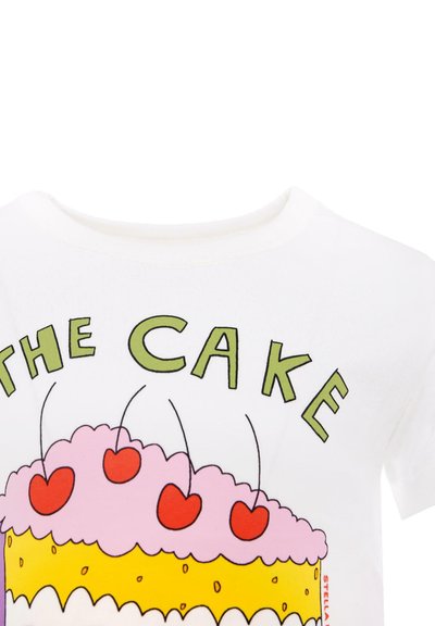 T-shirt en coton blanc avec un graphique de gâteau coloré, recouvert de glace rose, garni de cerises rouges et de couches jaunes. Le texte indique "LE GÂTEAU" en vert.