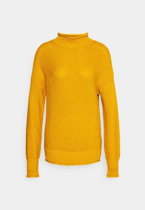 Pull jaune en maille avec manches longues et col montant côtelé sur fond gris clair.