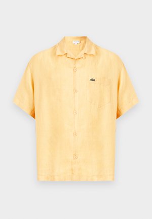 Cămașă galbenă cu mâneci scurte, cu nasturi, guler și buzunar la piept cu un mic logo al unui crocodil verde.