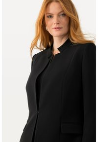 Schwarzer Blazer mit hohem Kragen, strukturiertem Design und Fronttaschen. Glatte Textur mit taillierter Passform, geeignet für formelle Anlässe.