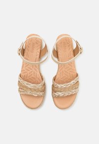 Sandalias marrones con tiras de paja trenzadas, cierre de hebilla en el tobillo y plantilla texturizada con un patrón de hojas. Esquema de color claro y neutro.