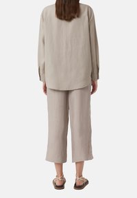Hellbeige Leinenhemd mit lockerer Passform und langen Ärmeln, kombiniert mit passenden Cropped-Hosen und Riemchensandalen. Glatte Textur, minimalistisches Design.
