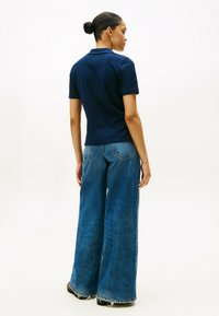 Granatowa koszulka polo z bawełny, z krótkimi rękawami i kołnierzykiem, zestawiona z niebieskimi dżinsami o wysokim stanie i szerokich nogawkach z postrzępionymi brzegami.