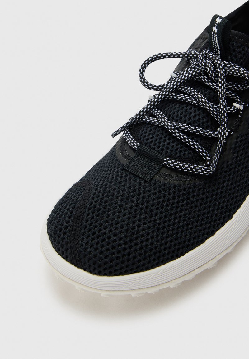 Zapato atlético de malla negra con cordones en contraste en blanco y negro, parte superior texturizada, suela de goma y diseño minimalista.