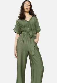 Mono verde hecho de tejido ligero, con cuello de solapa, mangas cortas, cintura ceñida con cinturón y piernas anchas.