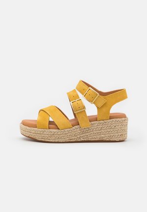 Sandale compensée en daim jaune avec deux brides réglables à boucle et une semelle plateforme en jute tressée.