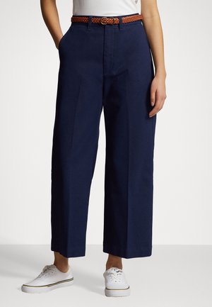 Navy wide-leg trousers with a smooth texture, featuring a braided brown belt and front pockets, paired with white sneakers.