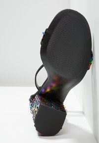 Sandalia negra con un tacón de bloque texturizado y multicolor. La suela tiene una superficie acanalada para un mejor agarre, mostrando intrincados adornos en el tacón.