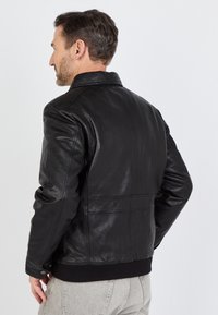 Zwarte leren jas met een gladde textuur, ribbelzoom en een klassieke kraag, voorzien van zichtbare stiklijnen en een getailleerde pasvorm.