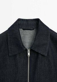 Dark denim jacket with a classic collar, metal zipper closure, and textured fabric. Features a clean, straight cut and minimal detailing.