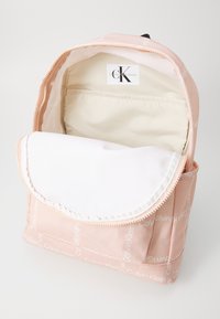 Calvin Klein rožinis nailono kuprinė su užtrauktuku, balto vidinio pamušalo ir logotipo spaudos akcentais. Suapvalintas viršutinis dangtis ir erdvus vidus.
