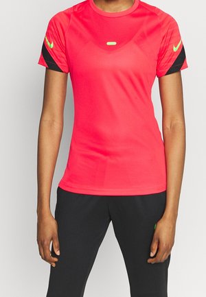 Frau trägt ein leuchtend rotes kurzärmeliges Sportshirt mit schwarzen und neongrünen Akzenten, kombiniert mit schlichten schwarzen Hosen.