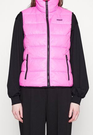 Roze gewatteerd mouwloos vest met voorrits en zakken, gedragen over een zwart langarmshirt en zwarte broek bij een staande persoon.