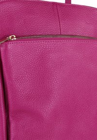 Helderroze gestructureerde leren tassectie met een gouden ritssluiting aan de bovenkant, waarbij de fijne nerf en stiksels goed zichtbaar zijn.