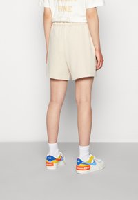 Ljust beige shorts med resårmidja, i kombination med färgglada sneakers med blå, röda och gula accenter. Vita ankelsockor synliga.