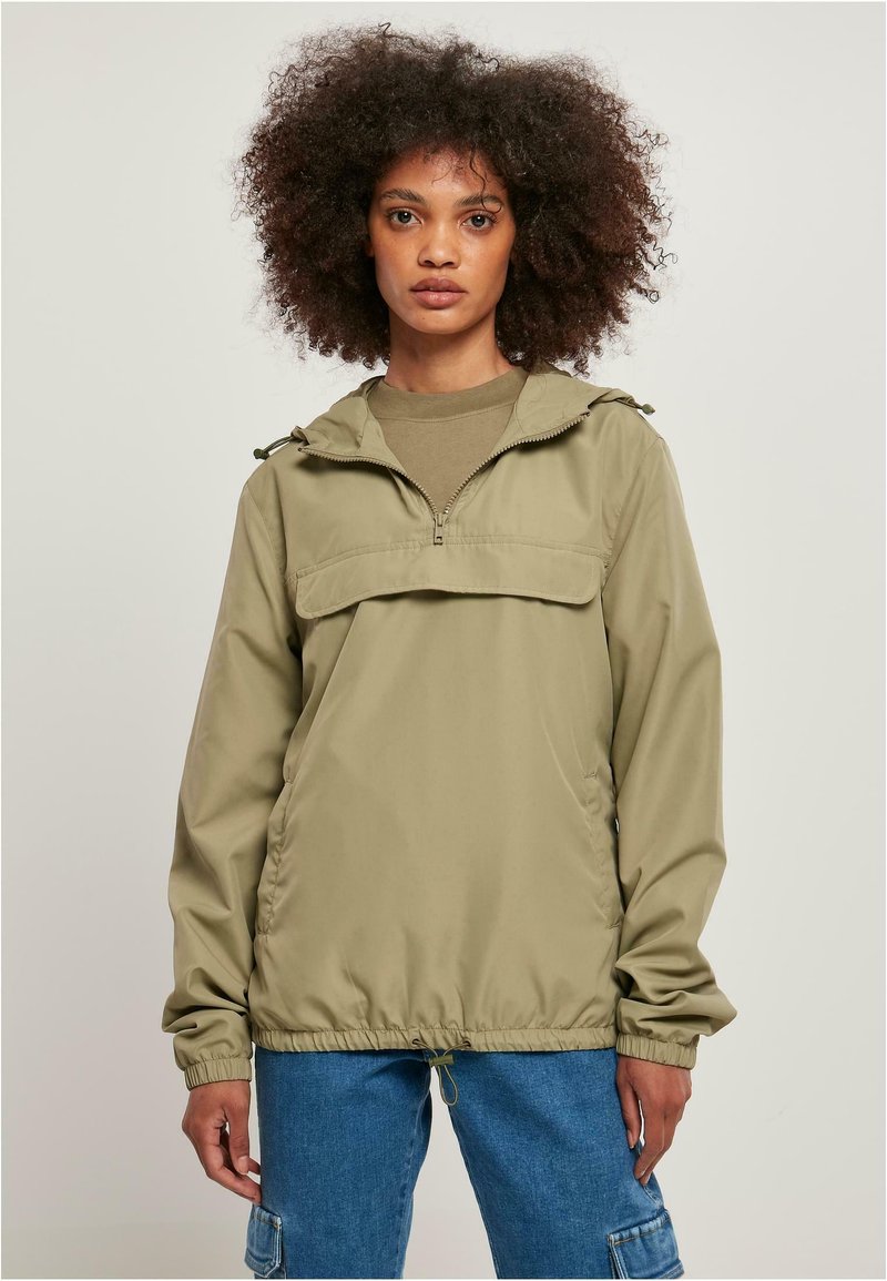 Khaki vindjakke med halv-zip-design, elastiske mansjetter og justerbar hette. Glatt tekstur og avslappet passform, kombinert med denim cargo-bukser.