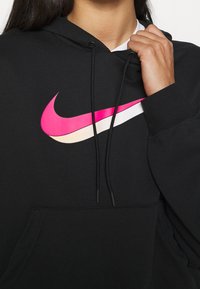 Černá mikina s kapucí s velkým, vícebarevným logem Nike v růžové a bílé barvě. Materiál je měkký, s nastavitelnými šňůrkami a přední kapsou.