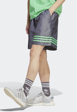 Pantaloncini grigi con dettaglio a striscia verde, realizzati in materiale leggero. Abbinati a sneaker grigie e bianche e calzini a righe.