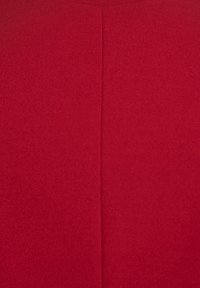 Czerwony materiał o gładkiej, matowej fakturze, z centralnym szwem i prostym wzorem, podkreślający minimalizm i bogaty kolor.