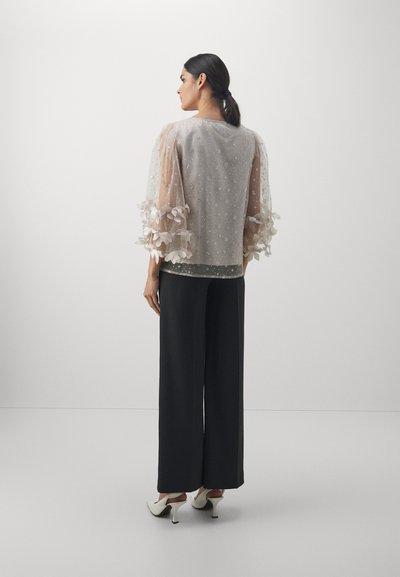 Lightweight, sheer, beige top with floral embroidery and puff sleeves, paired with black wide-leg trousers and white high-heeled shoes.