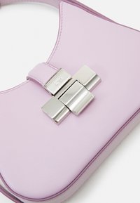 Kompaktowa torebka z jasnofioletowej skóry o błyszczącym wykończeniu. Posiada srebrną metalową klamrę i gładki, zaokrąglony kształt.