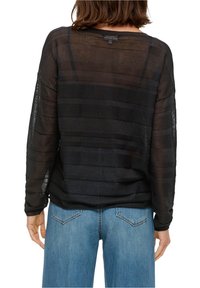 Svart transparent tröja med horisontell randig textur och vid halsringning, kombinerad med ljusblå denimjeans, sedd bakifrån.