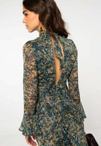 Mujer con un vestido de manga larga de estampado de leopardo, con la espalda descubierta y un lazo en el cuello, llevando grandes pendientes de oro.
