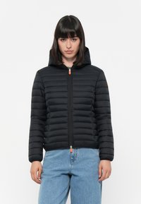 Zwarte gewatteerde jas met capuchon, gestikt ontwerp, vooraan met een rits en een oranje ritslip. Beschikt over elastische mouwen en een slim fit.