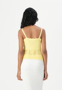 Kollane heegeldatud crop top, millel on lainelised servad ja õhukesed rihmad, ning tekstuuriga alumine osa. Kanda koos valge tekstuuriga seelikuga.