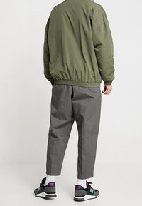 Olijfgroene bomberjack, grijze broek, zwarte sneakers met paarse accenten. Glad materiaal, comfortabele pasvorm, elastische manchetten en tailleband.