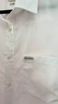 Vit bomullsskjorta med krage, med en enda frampocket och en "Guess Jeans"-etikett. Knapparna är runda och gjorda av plast.