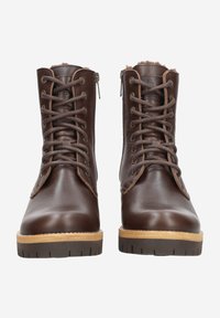 Bottes basses en cuir marron avec fermeture à lacets sur le devant, fermetures éclair latérales, et une semelle en caoutchouc brun clair avec un motif texturé. Doublure en fausse fourrure visible.