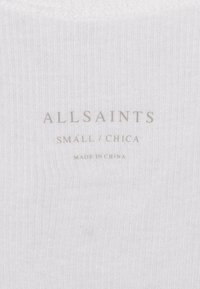 Hvid ribbet stof med "ALLSAINTS" logo trykt i lys grå. Størrelse angivet som "SMALL/CHICA." Etikken angiver "LAVET I KINA."