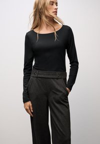 Schwarzes langärmeliges Oberteil mit Rundhalsausschnitt, kombiniert mit hochtaillierten, dunkelgrauen, weiten Hosen, die zwei Fronttaschen und Knopfakzente aufweisen.