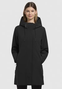 Manteau imperméable noir avec capuche, poches zippées et cordons de serrage réglables. Présente un design élégant et minimaliste ainsi qu'une texture lisse.