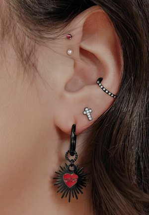 Schwarze Ohrringe mit einem Herzanhänger, der rote Akzente und Spitzen aufweist, ergänzt durch silberne Akzente anderer Ohrlöcher.