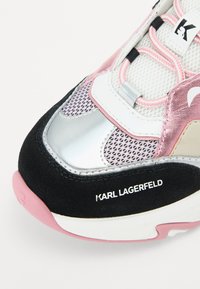 Fekete velúr alapú sneaker, ezüst és rózsaszín díszítéssel, hálós panelek, valamint kiemelkedő logó. Jellemzője a kerek forma és a texturált dizájn.