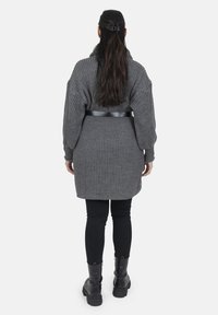 Grå strikket cardigan med lange ærmer, bælte i taljen, set bagfra. Båret over sorte leggins og ankelstøvler. Glat, struktureret stof.