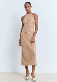 Vestido midi nude con lentejuelas, escote halter, forma ajustada, textura suave y un elegante caído, combinado con tacones abiertos blancos.