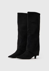 Para czarnych zamszowych kozaków sięgających do kolan z ostrymi noskami i niskimi obcasami typu kitten heels na białym tle.