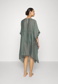 Poncho leggero verde chiaro, trasparente, con bordo asimmetrico e dettagli a frange. Presenta un collo semplice e un design libero e fluido.