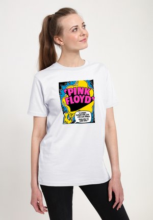 Kvinde med brunt hestehale iført hvid t-shirt med farverigt Pink Floyd-grafik og tekst, kigger op og til siden.
