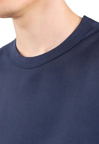 Mörkblå t-shirt med rund halsringning, tillverkad av mjuk och slät bomullstyg; den har en ribbad halsringning och en enkel, minimalistisk design.