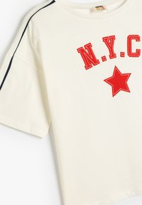 Cremefarvet bomulds-t-shirt med rødt "N.Y.C." tryk og stjerne grafik, med marineblå sideløse og korte ærmer.
