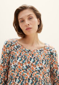 Bluse mit Blumenmuster aus leichtem Stoff; in orange, teal und blauen Farbtönen, mit Rundhalsausschnitt und Knopfakzenten.