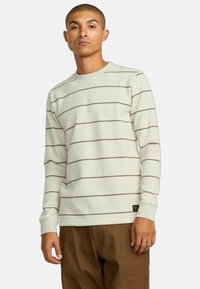 Langarm, ribbelde crewneck shirt in gebroken wit met bruine horizontale strepen. Voorzien van een klein logo label aan de zoom.