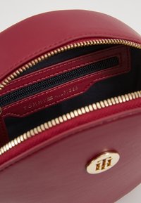 Borsa rotonda in pelle rossa con zip dorata e tasca interna con logo. Foderata in tessuto nero, presenta un accento in metallo con il logo.