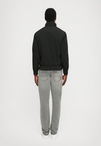 Sort bomberjakke med høj krave, parret med lysegrå tapered jeans og hvide sneakers. Glat stof med en afslappet pasform.