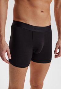 Svarta boxerkalsonger gjorda av mjukt tyg, med en elastisk midjeband som har "JES UNDERWEAR"-logotyp, åtsittande passform och slät textur.